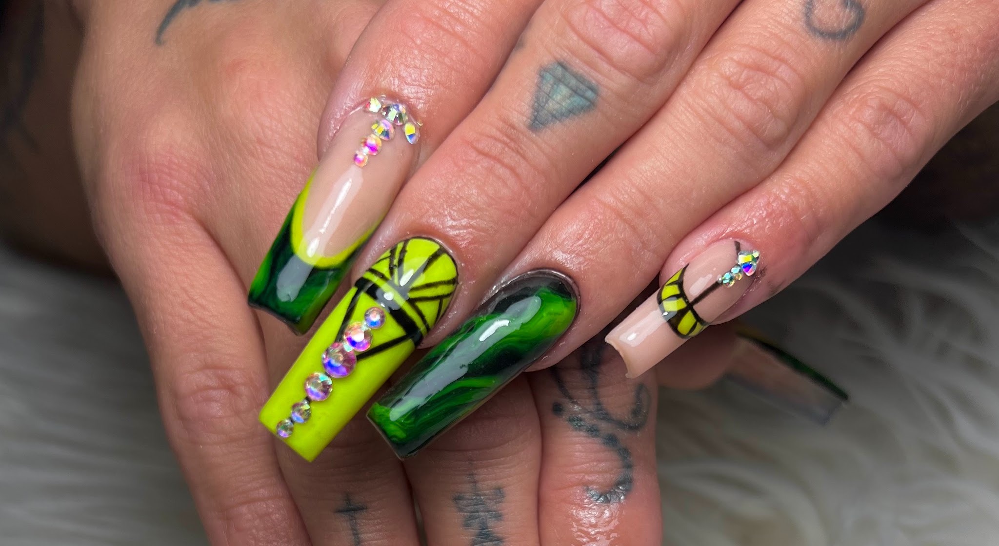 Neongroene en zwarte nail art met strass op een getatoeëerde hand