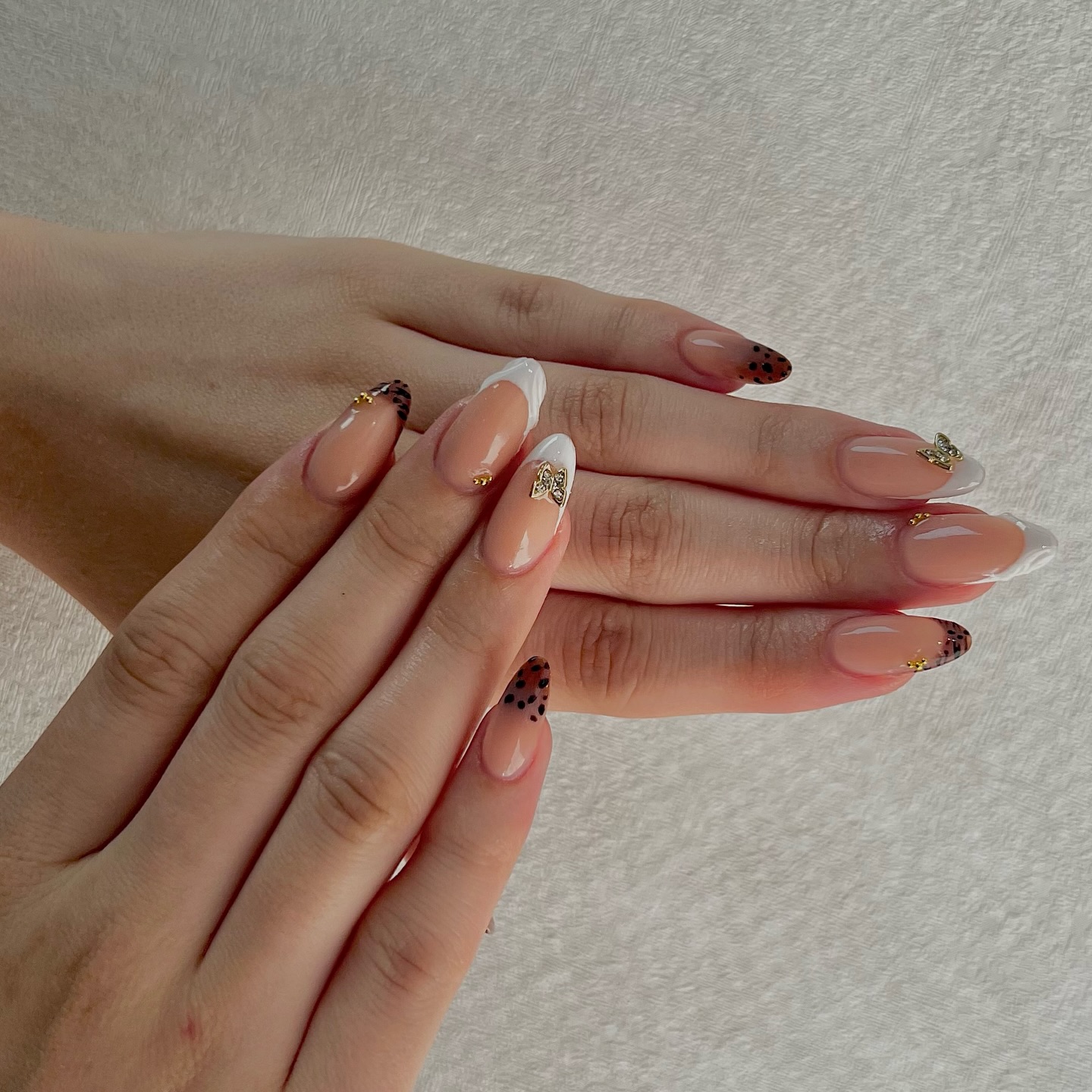 Natuurlijke almond nagels met witte French, gouden charms en bruine stippen